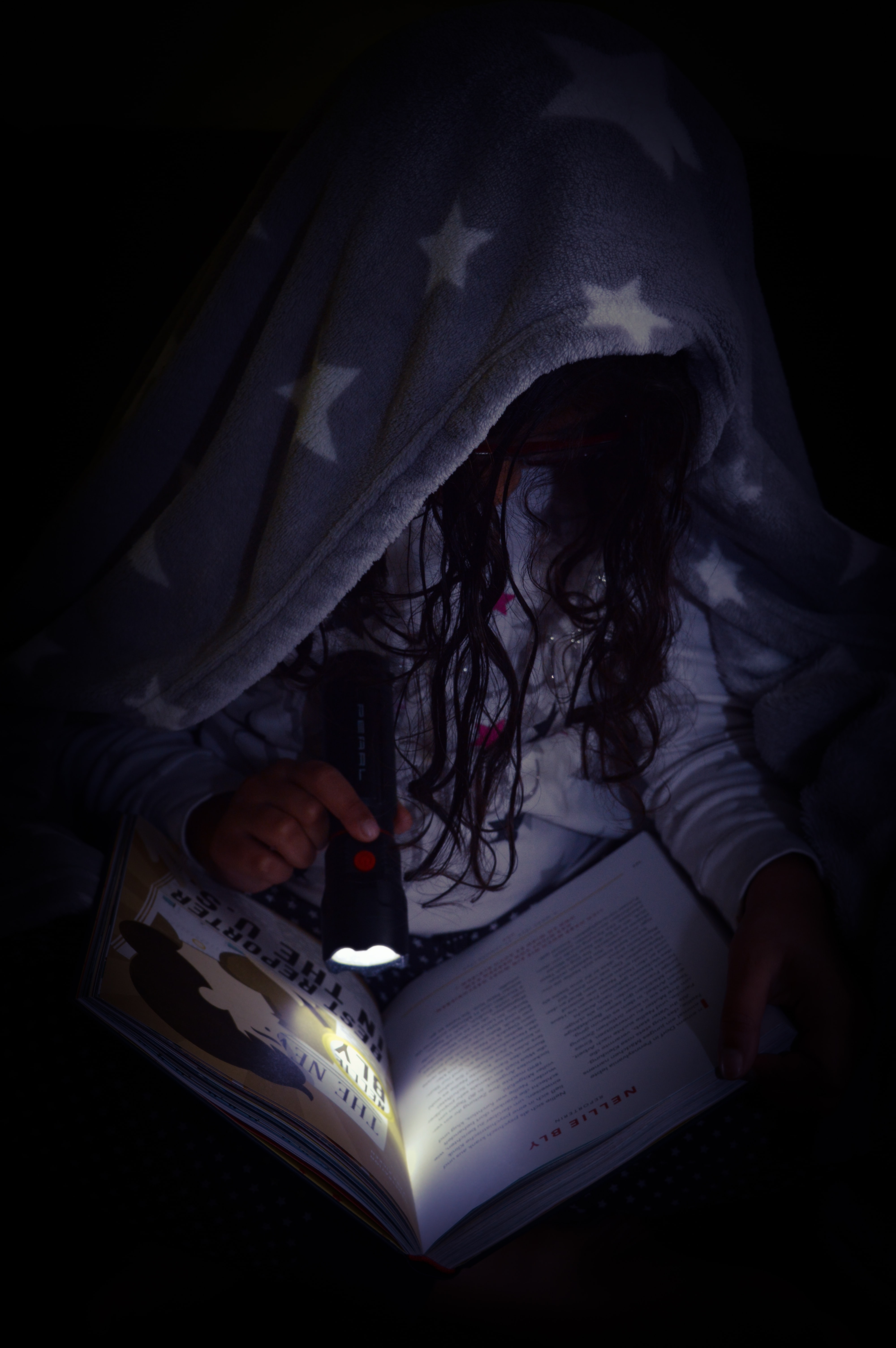 Bild på ett barn som läser en bok under en filt